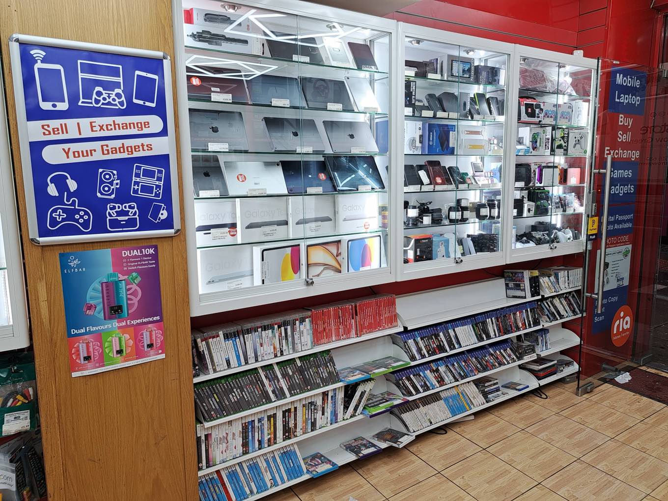 Glass cabinets of tablets, gadgets and accessories with a wall of pre-owned games at DIGICOM